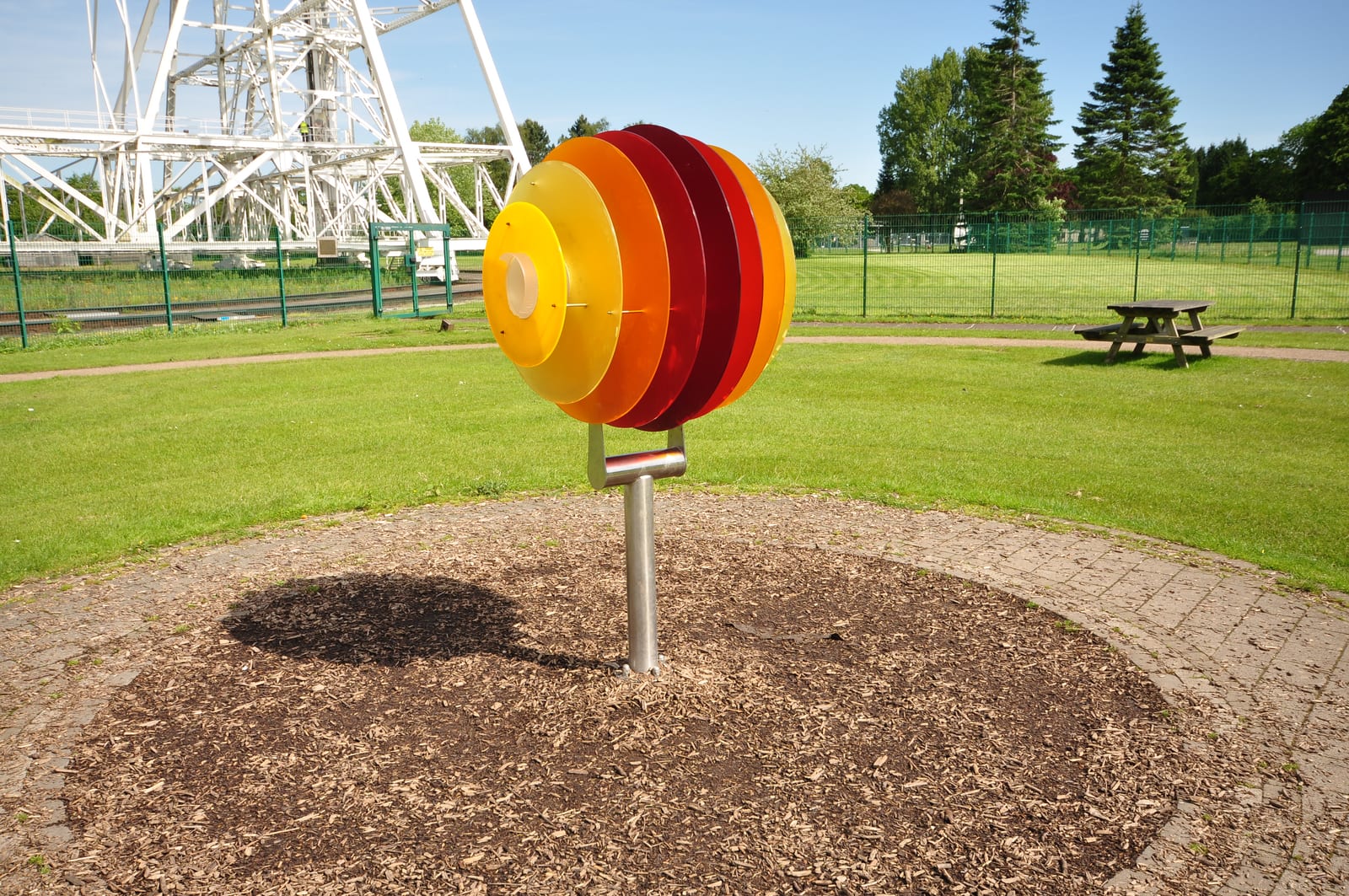 A red, orange and yellow Solar System model stands on the grass near the Lovell Telescope structure.